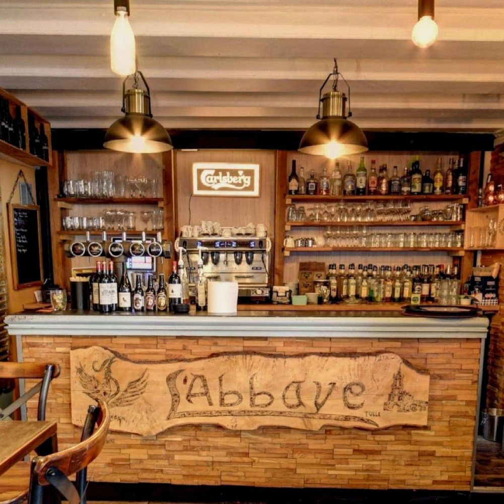 Comptoir en bois gravé du bar de L'Abbaye, lampes en cuivre suspendues.