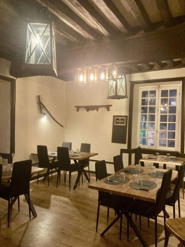 Salle intérieure de L'Abbaye, plafond à poutres apparentes, lanternes en métal noir, tables dressées.